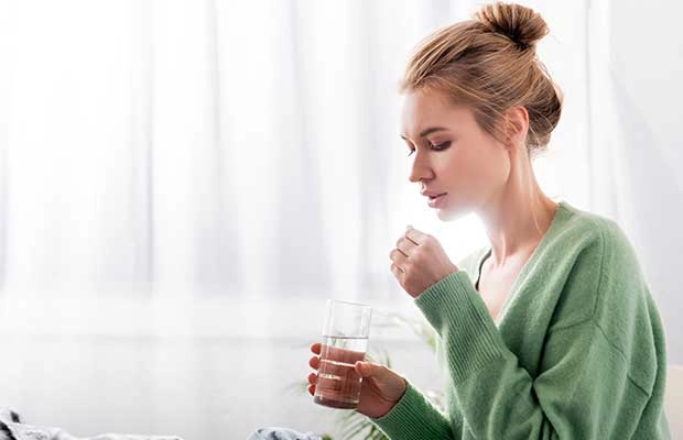 Woman taking weight loss pill with a glass of water
